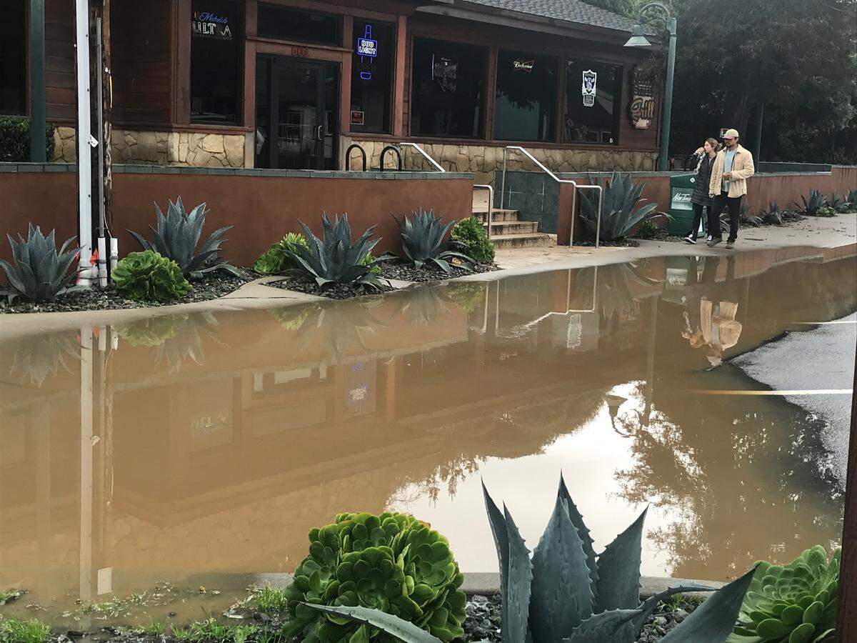 Visitors from Santa Barbara walk past flooding in front of Main Street Grill in Cambria on Sunday, Jan. 8, 2023.