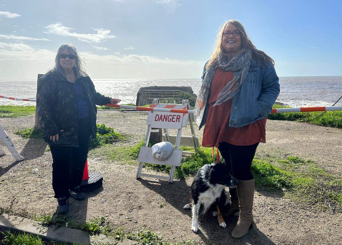 Effie McDermott, left, and Krista Oliver pose next to the bench in Margo Dodd Park in Shell Beach that is falling off the cliff on Jan. 10, 2023.