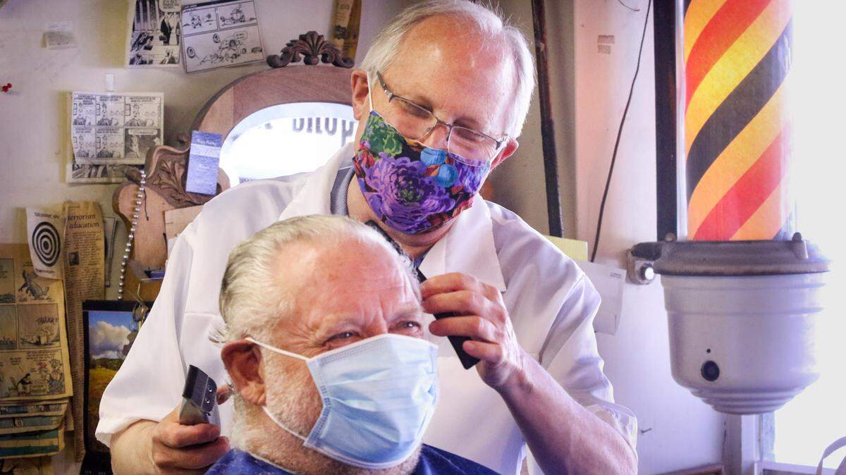 In this file photo, Ray Shearer is giving a haircut to his client Bob Nichols. California’s workforce safety board is discussing whether to pull back its mask and social distancing requirement at workplaces.