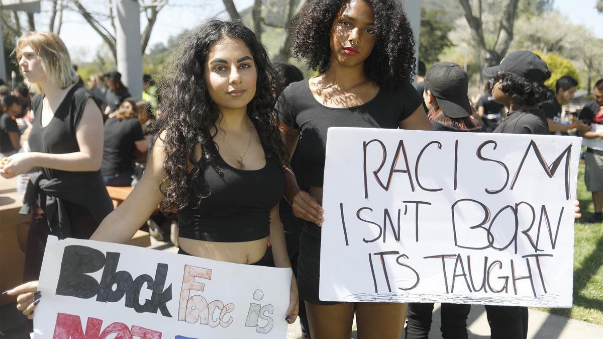 Two students, Ariana Afshar, left, of Cal Poly, and Tianna Arata, of Cuesta College, hold signs during a silent march Saturday, April 14, 2018, during the annual Cal Poly Open House in protest of the university's response to a fraternity member pictured wearing blackface. They marched from campus to Santa Rosa Park in San Luis Obispo and held a picnic.