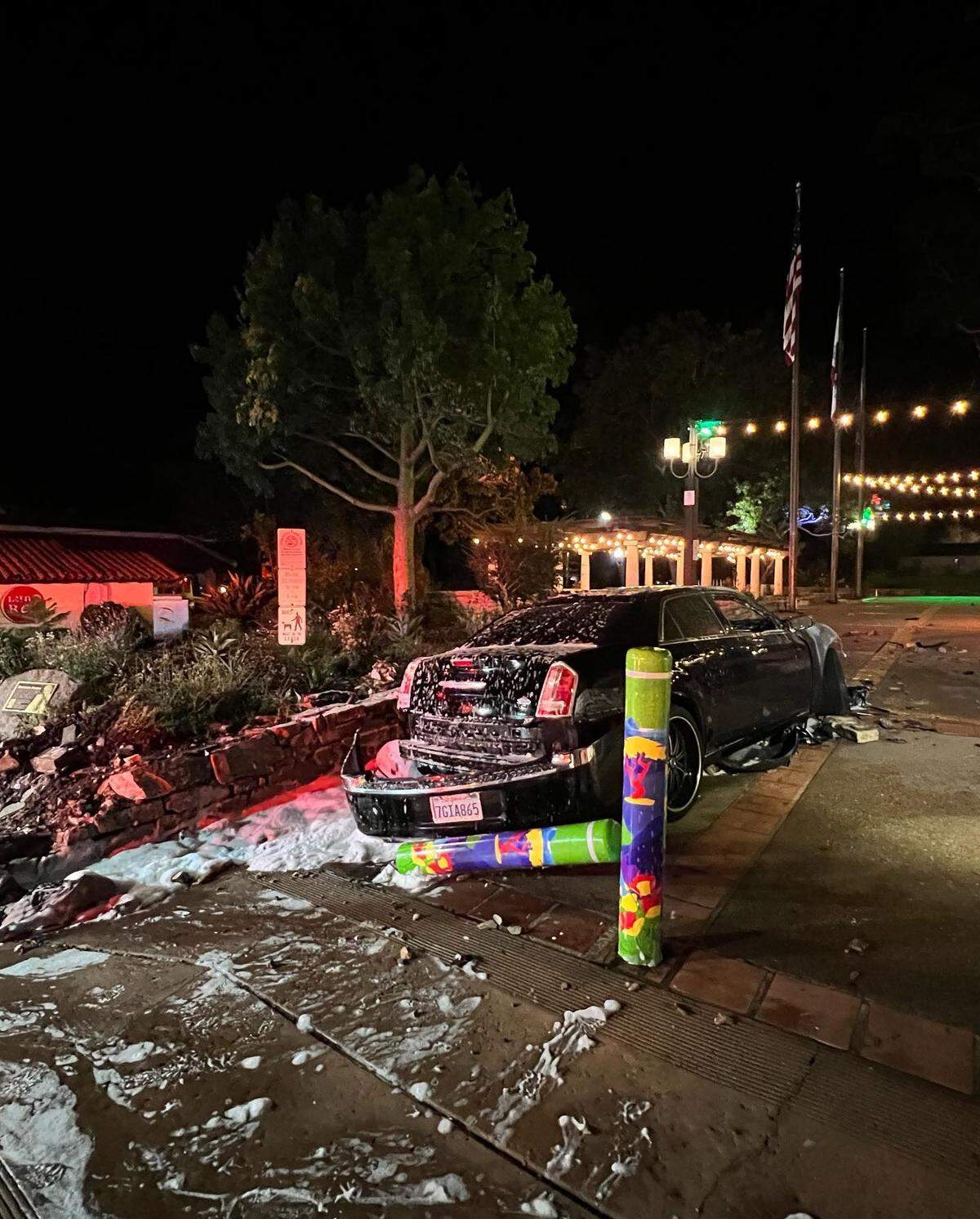 A car is covered in flame-retardant foam after crashing into the landscape wall and entrance bollard at Mission Plaza in downtown San Luis Obispo on Tuesday, Aug. 23, 2022.