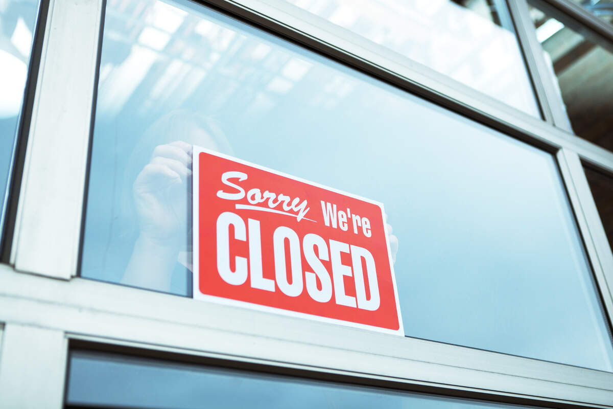 An employee posts a “Sorry, We’re Closed” sign in the window of a business.