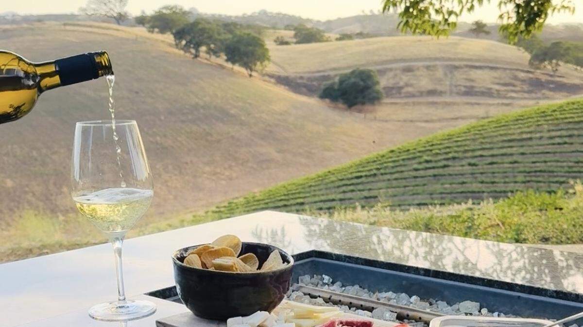A charcuterie board of cheeses, meats, olives and chips accompany a glass of wine.