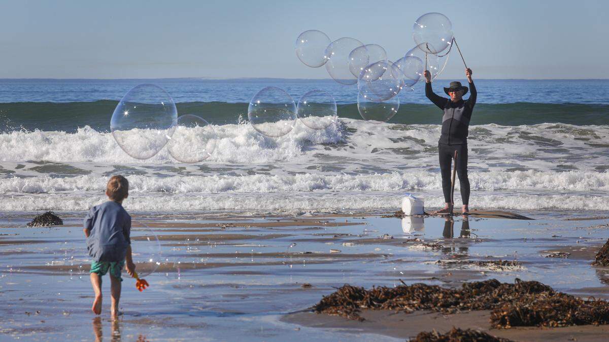 Carter Charpentier, 7, found his sand rake perfect for chasing bubbles created by Phil Hinton. They were at Pismo Beach on Monday morning about the time the high tide peaked.