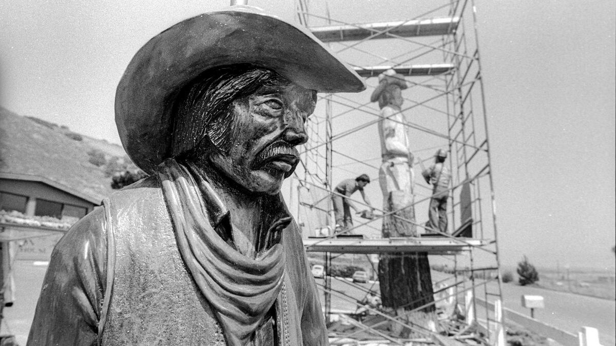 A sculptor uses a carved lamp, left, as a model for Clint the rugged cowpoke at McLintocks Saloon and Dining House in Pismo Beach. A dead Monterey pine was carved into the landmark Clint the cowboy in June 1983.