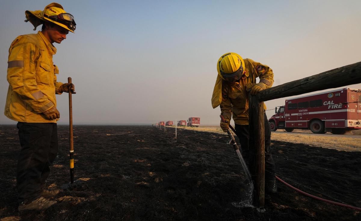 Monterey County firefighters Jonathan Davis, left, and Ryan Cahalan extinguish smoldering wood posts on a cattle fence along Soda Lake Road after the Madre Fire burned through the area on July 3, 2025.
