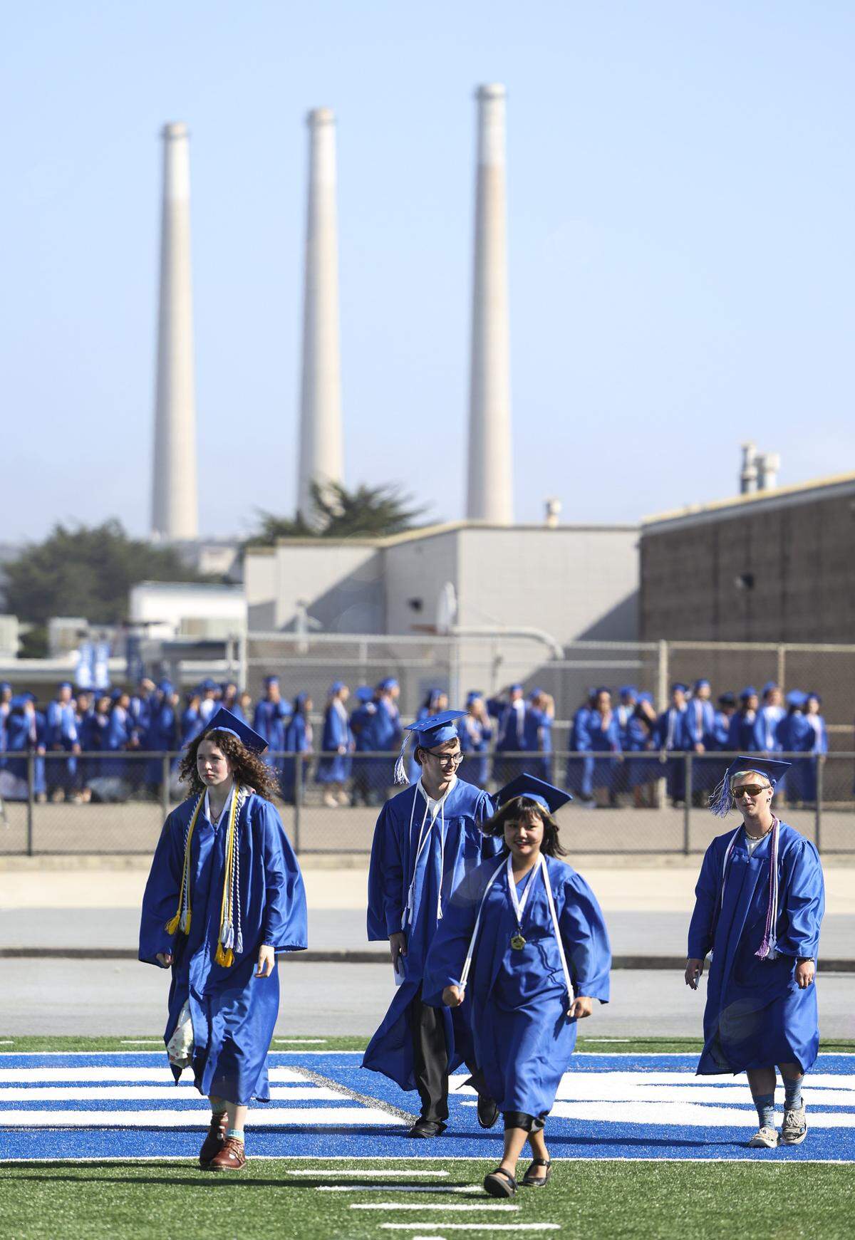Students enter the football stadium with the power plant smoke stacks in the background. Morro Bay High School issued diplomas to 176 graduates on June 4, 2026.