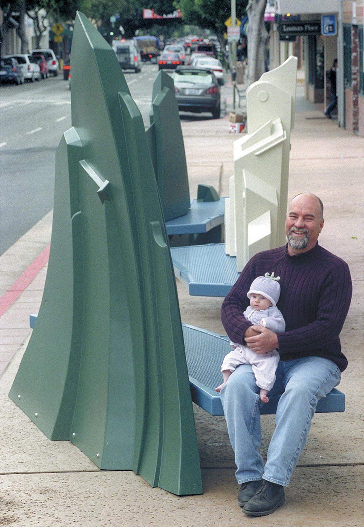 Metal artist Allen Root with his artwork that graces his hometown. These benches were on Higuera Street near Osos Street. Pictured on Jan 11, 2001, holding his daughter Lilianna, 3 months. The benches echo the shapes of the peaks, the city and the creek. The benches were removed when the Court Street project got underway.