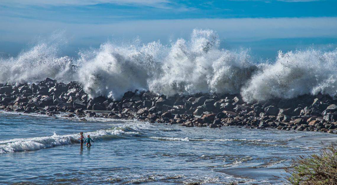 Two children play in the calmer waters of the Morro Bay Harbor on New Year’s Day as huge waves crash over the jetty behind them. Their guardians were nearby, just up the shore.