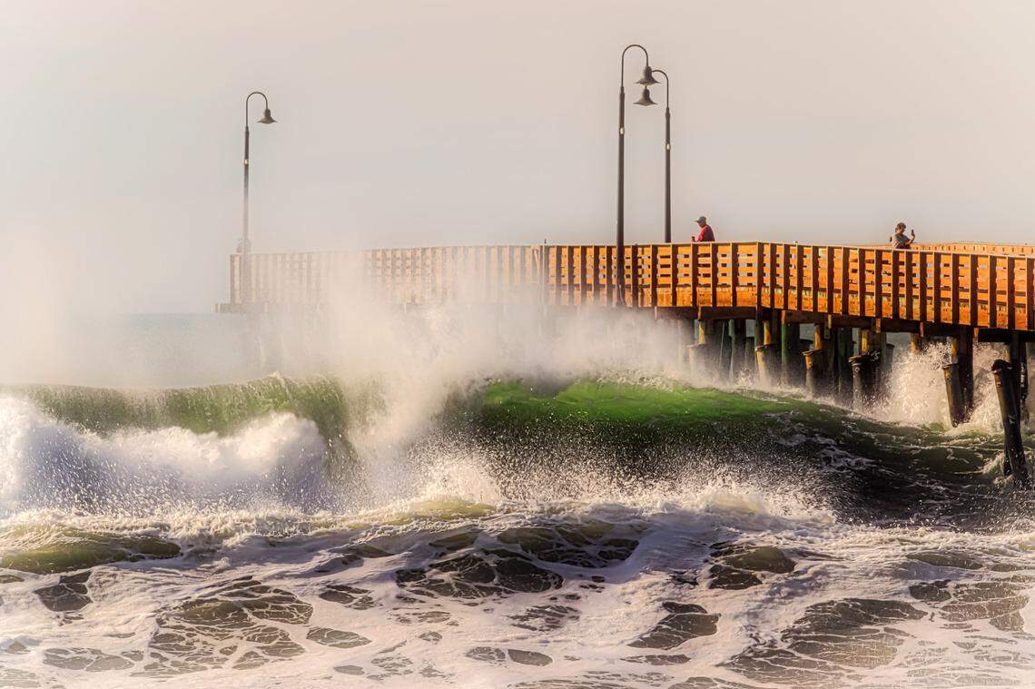Big waves crash onto the beach next to the Cayucos Pier.