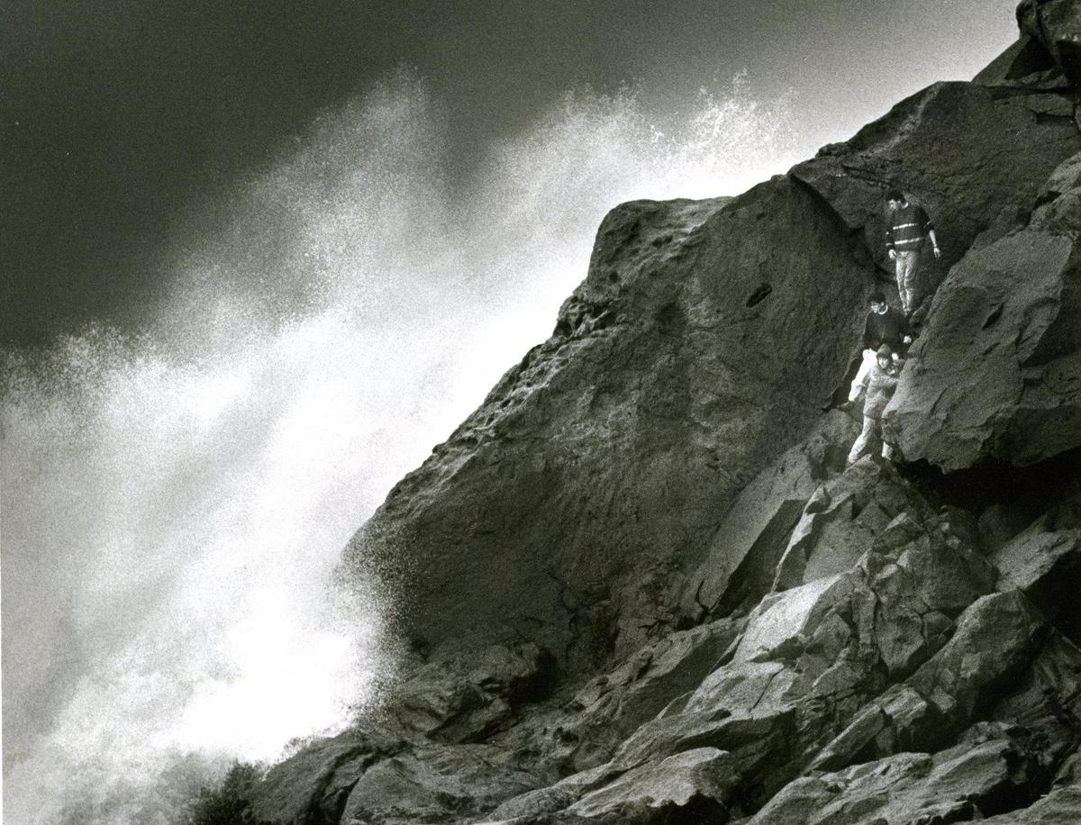 A threeesome clings to rocks above crashing surf on the seeward side of Morro Rock, above the Morro Bay breakwater in this photo published March 4, 1991.