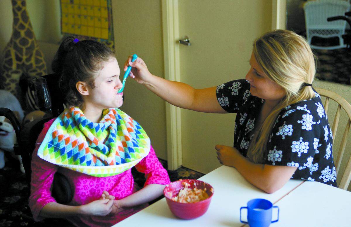 Blair Gracey, a certified nursing assistant, feeds Emonee, one of the children at Sjany de Groot’s former nursing home in San Luis Obispo.