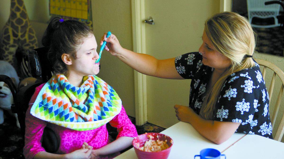 Blair Gracey, a certified nursing assistant, feeds Emonee, one of the children at Sjany de Groot’s home in San Luis Obispo.