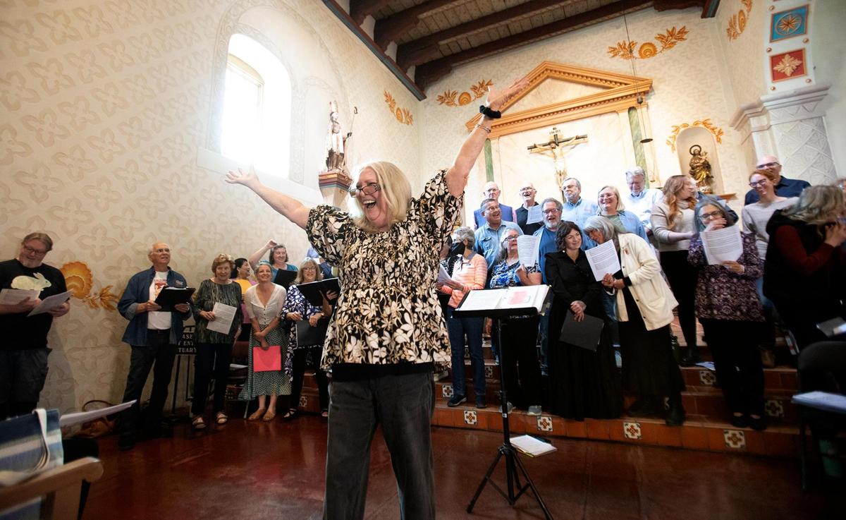 Musical director Melody Svennungsen encourages the packed Mission San Luis Obispo to sing along at a special event on Feb. 24, 2024, to honor longtime choir director Gary Lamprecht, who died on Wednesday.