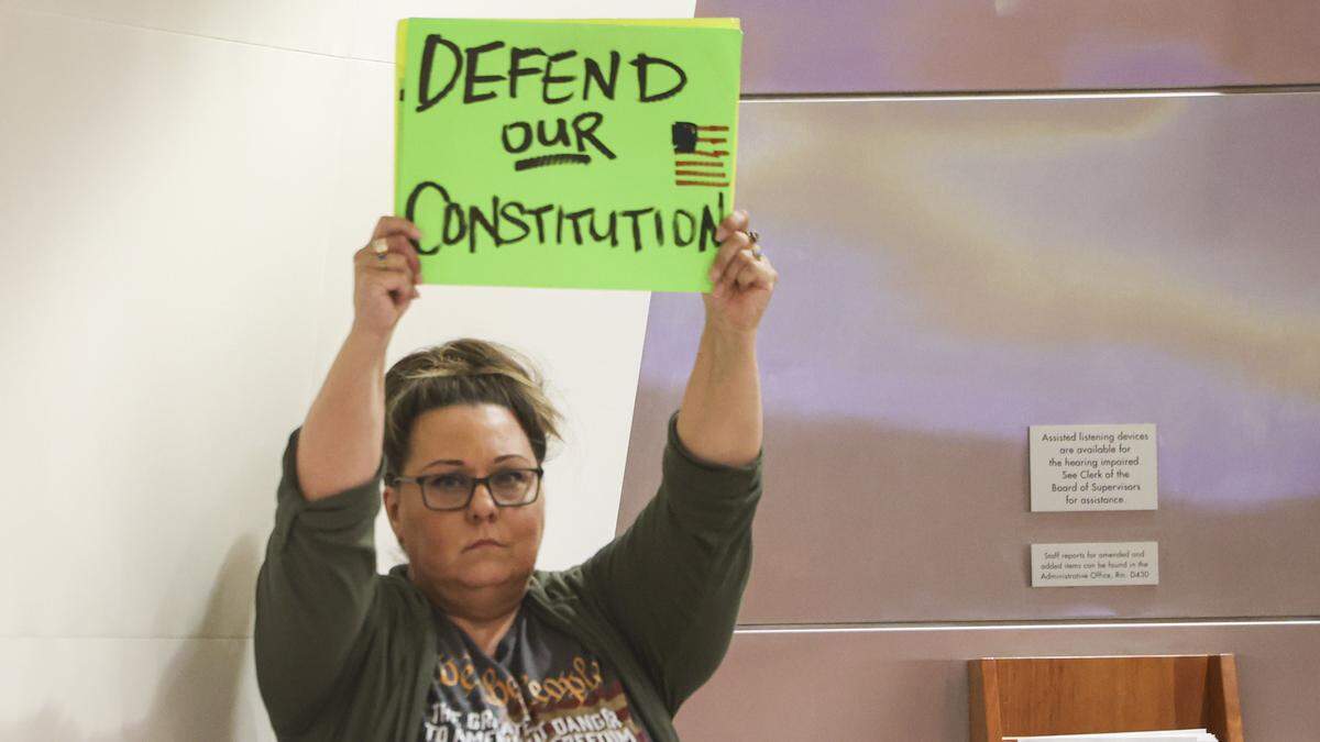 Jeannette de la Cruz silently held a sign. The San Luis Obispo County Board of Supervisors took public comment and official presentations on a controversial federal grant, seen here on Aug. 5, 2025.