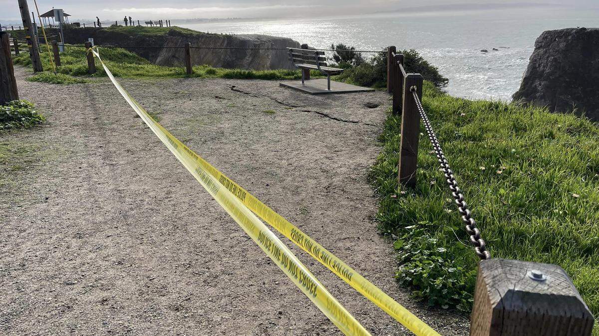 Caution tape strung across two wooden fence barriers at Margo Dodd Park in Pismo Beach due to a large crack in the ground.