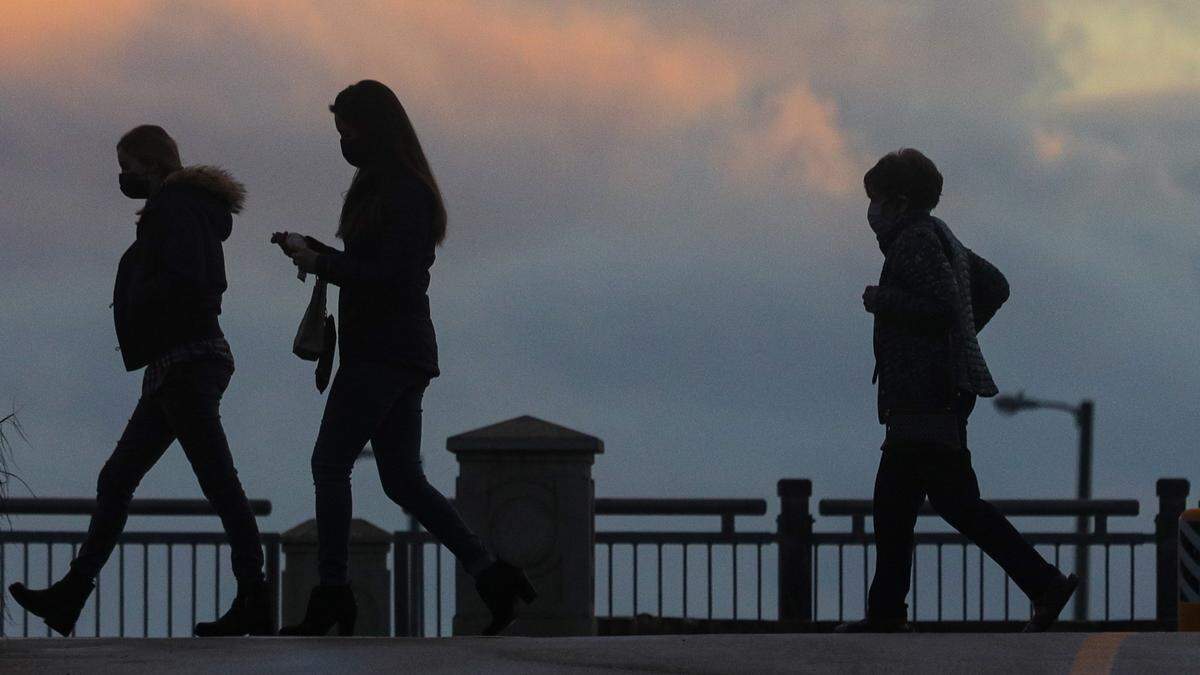 Pedestrians walk along Front Street in Avila Beach as the sun sets behind rain clouds on Monday, Dec. 27, 2021.
