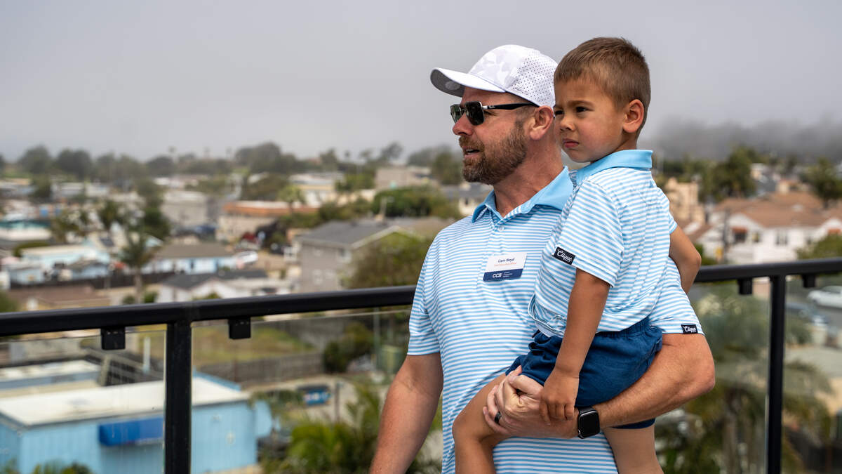 Coastal Community Builders CEO Cam Boyd holds his son Bronson on the rooftop of the 59-unit “Encore” project on West Grand Avenue during its grand opening on June 13, 2026. Visitors were invited to tour the lobby, rooftop, units and amenities of both buildings.