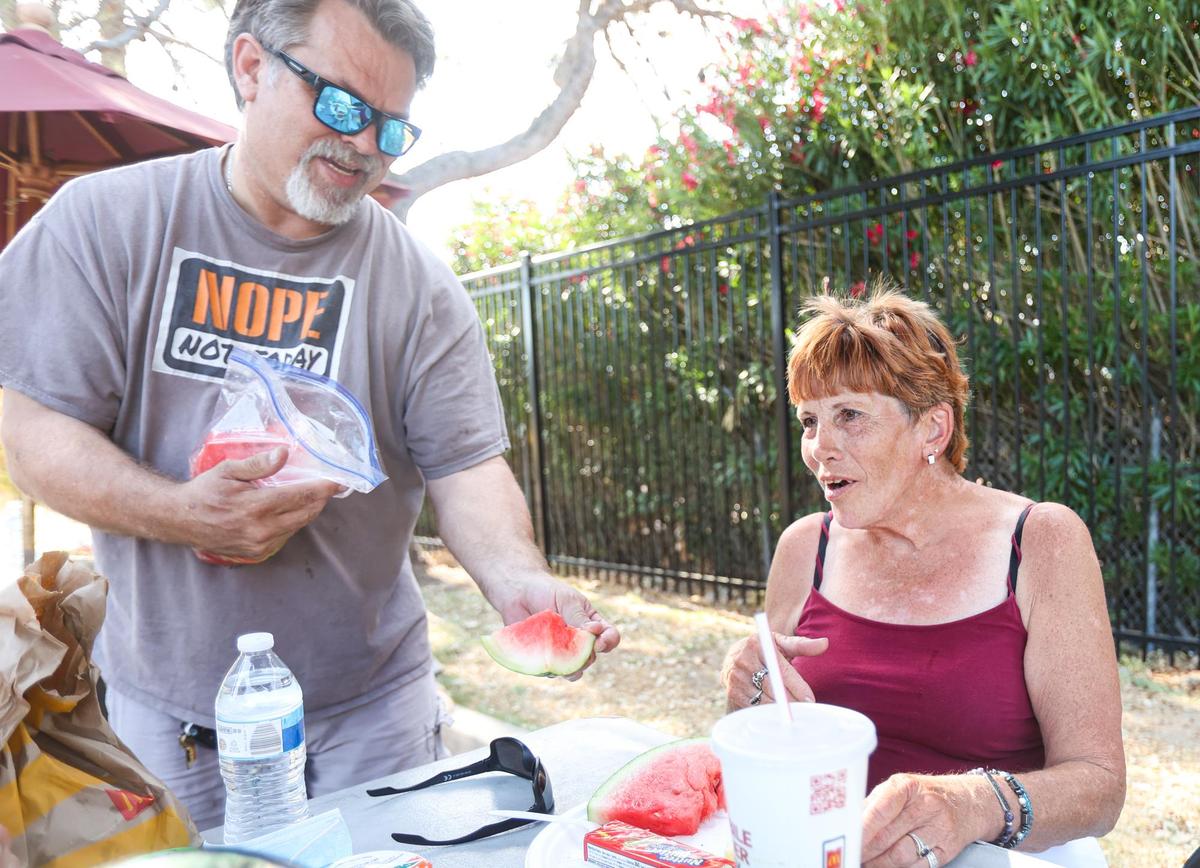 Volunteer Greg Heim gives a watermelon slice to Christina Gragg at an evening meal held at the ECHO shelter in Paso Robles. Three local nonprofits converted the former Motel 6 into an overnight facility and affordable housing in late 2020.