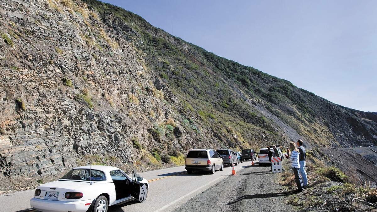 Traffic on Highway 1 is stopped near the site of last year’s landslide at Alder Creek on Wednesday as a helicopter lowers netting onto the hillside.