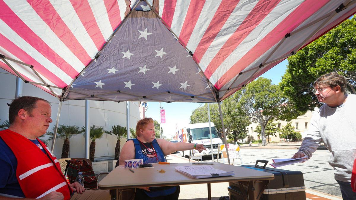 From left, poll workers Brian O’Connor and Katy Bertrand assist voters making sure envelopes are signed and dated, as Dennis Burns drops off his ballot at the San Luis Obispo County Government Center on June 7, 2022.