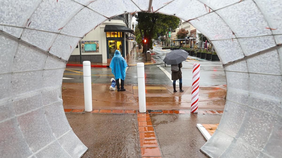 Pedestrians wait for the light to change at Chorro Street in a view framed by the holiday light tube at Mission Plaza. The rain continued to fall in downtown San Luis Obispo on Tuesday morning, Dec. 14, 2021.