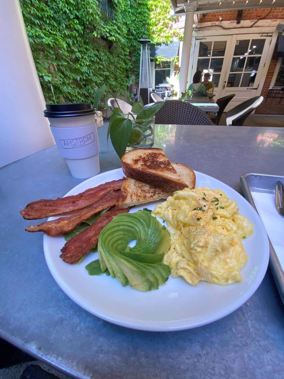 A breakfast plate featuring eggs, avocado and bacon is served in the ivy-lined courtyard at AMSTRDM Coffee House in Paso Robles.