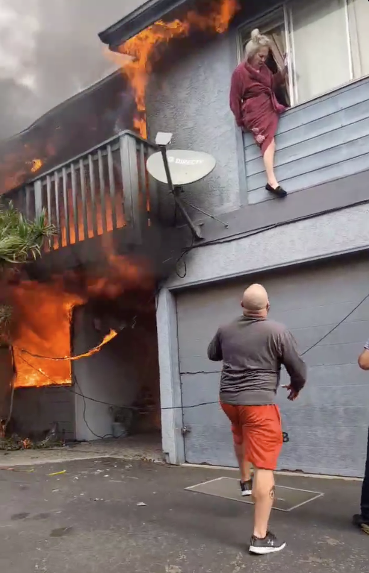 A woman climbs from a second-floor window to escape a fire burning an apartment in Grover Beach on Tuesday, July, 20, 2025.