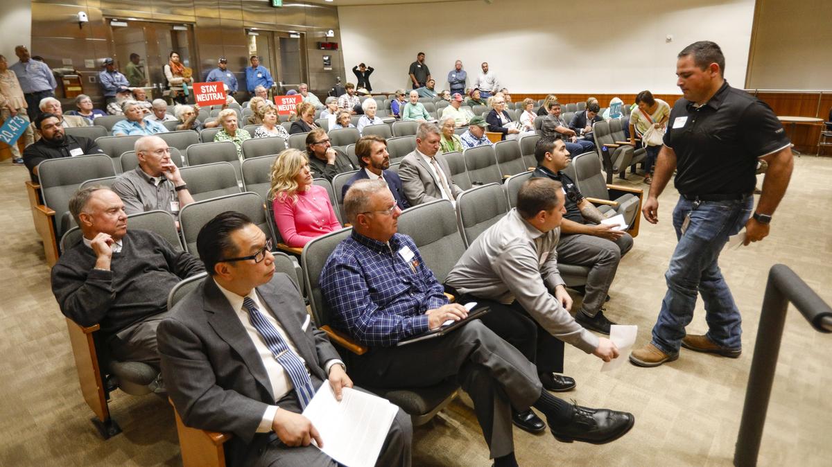 SLO County Auditor-Controller James Erb and Clerk-Recorder Tommy Gong, left, attended Tuesday's Board of Supervisors meeting to answer questions about the ballot measure on banning new oil wells and fracking. At right front are Phillips 66 refinery officials, including maintenance superintendent Jim Anderson, in blue shirt. Holding signs are supporters of the anti-fracking initiative.