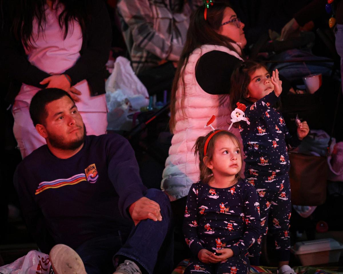 From left Ulysses Carbajal, Alessandra Carbajal, 4, Raynee Guiterrez and Chelsea Guitierrez, 2, waving to fire engines. Unseasonably warm weather encouraged a large crowd to attend the 48th annual downtown Holiday Parade. on Dec. 6, 2024.