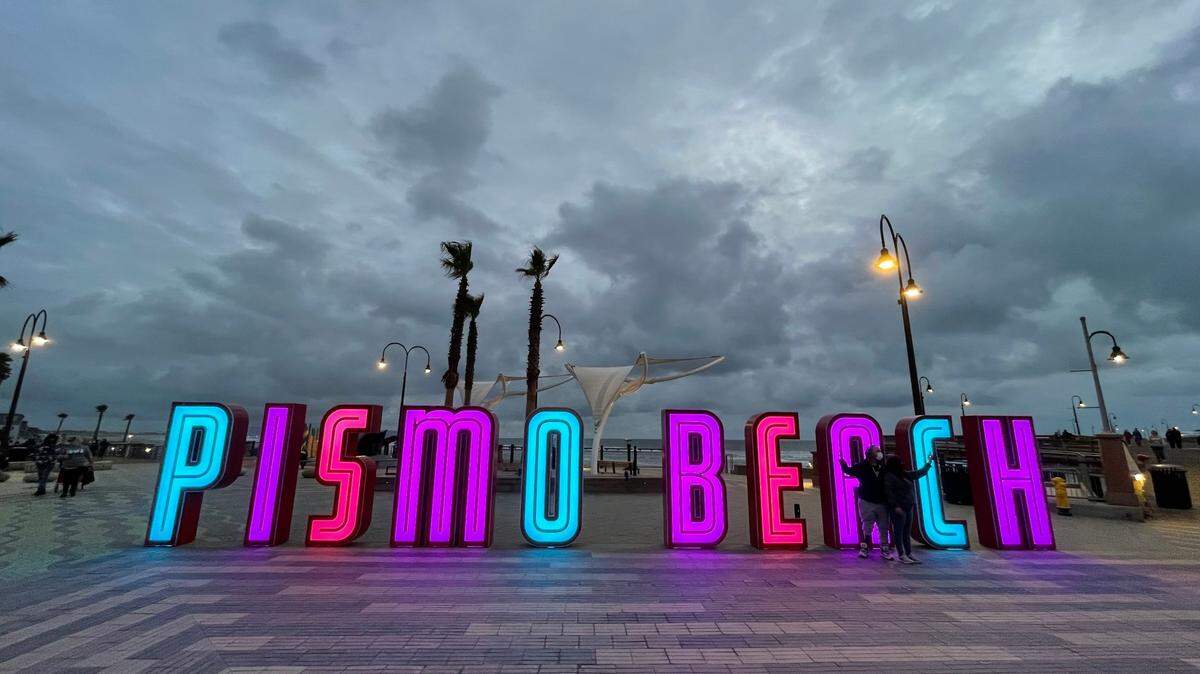 Visitors take a selfie in front of the lighted Pismo Beach sign as storm clouds roll in on Sunday evening.