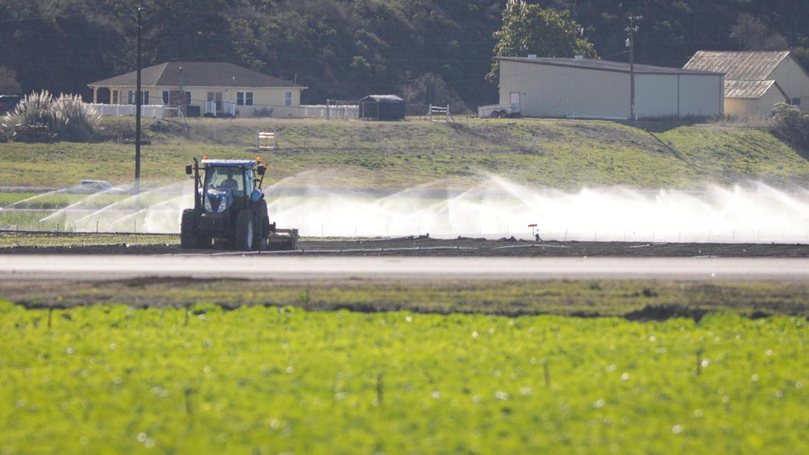 A tractor tills a field as irrigation sprinklers spray near Highway 1 and Halcyon Road in Arroyo Grande on Dec. 4, 2023.
