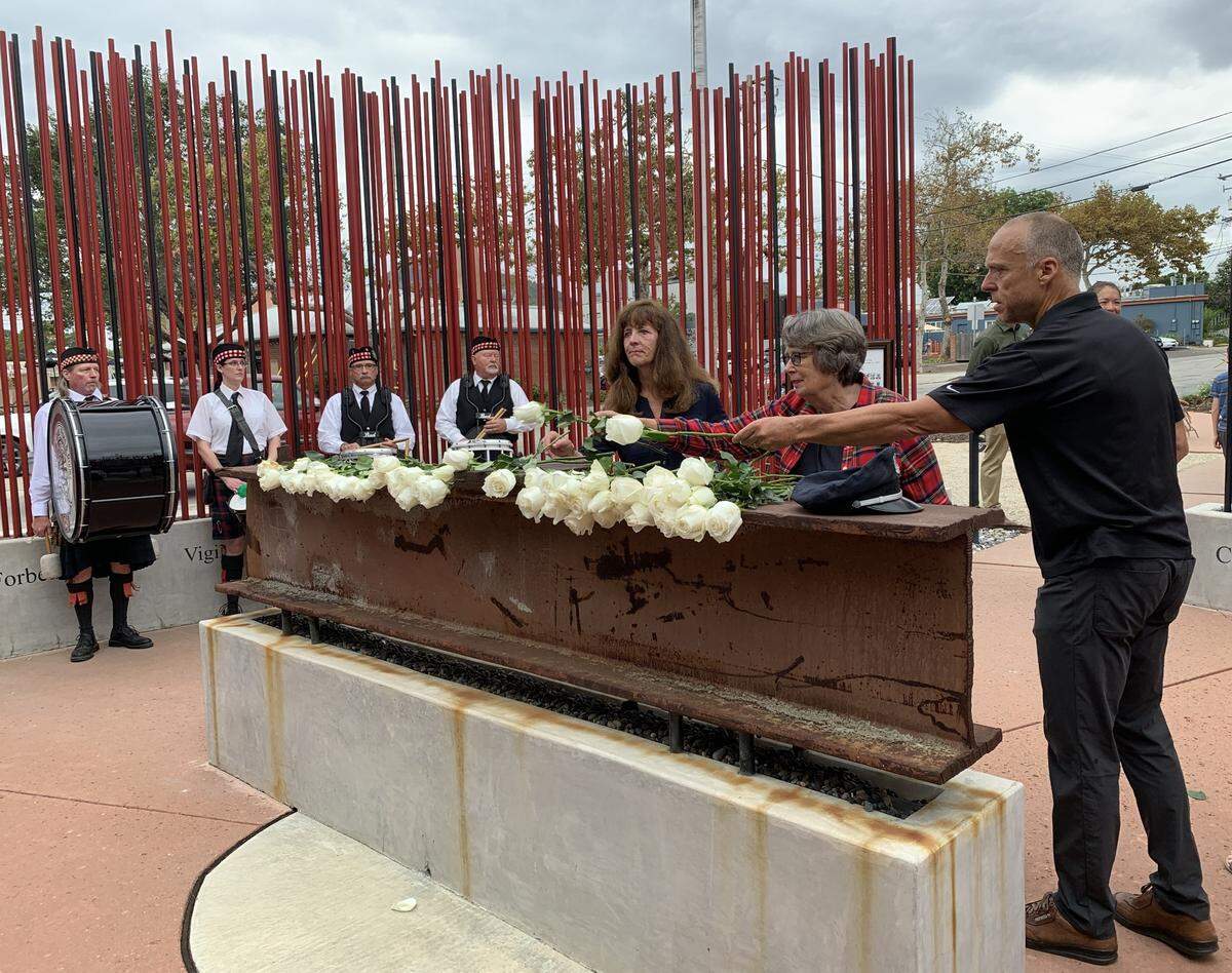 From left to right, San Luis Obispo teacher Mila Vujovich-La Barre, San Luis Obispo City Council member Jan Mark and San Luis Obispo city manager Derek Johnson lay white roses on the steel beam at the center of the World Trade Center Memorial in front of Fire Station No. 1 in San Luis Obispo on Sunday, Sept. 11, 2022, as members of Central Coast Pipes and Drums look on. The city held a 9/11&nbsp;Day of Remembrance ceremony at the site.