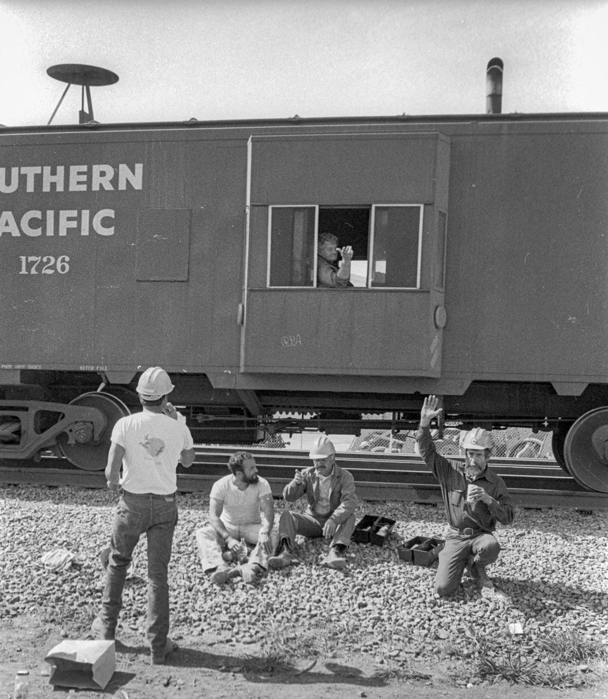 Workers on a lunch break wave to a passing Southern Pacific caboose in San Luis Obispo, Calif. on March 12, 1984.