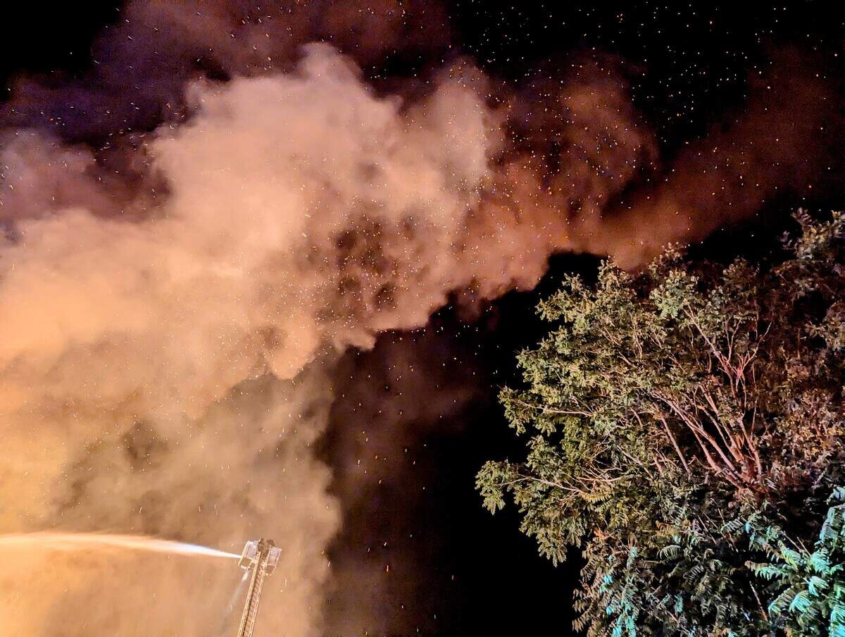 Smoke and glowing embers rise above nearby trees during the Feed & Grain fire on July 4, 2025. Embers threatened nearby vegetation and rooftops as firefighters worked to keep the blaze from spreading beyond the downtown business district.