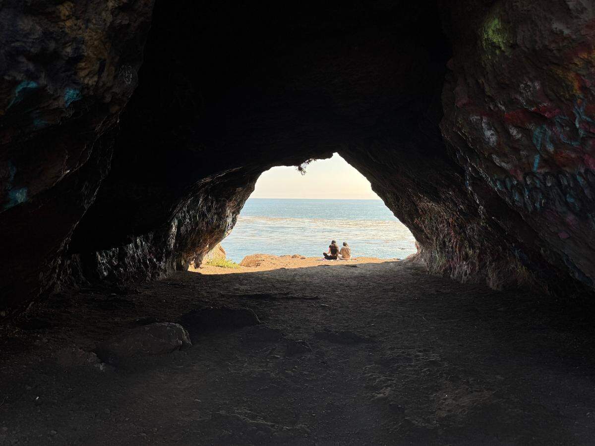 Two people sit in the mouth of Cave Landing on July 16, 2025.