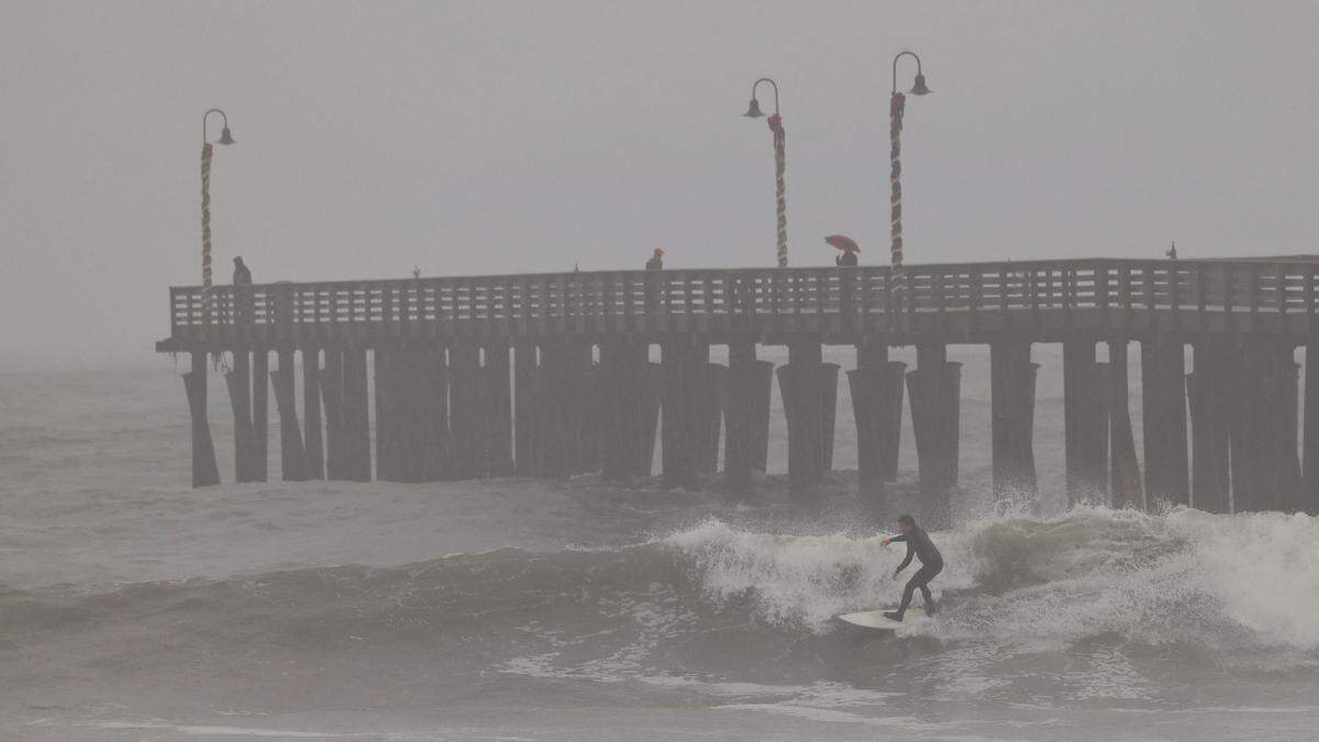 Surfers ply the waves in Cayucos during a rain storm on Tuesday, Jan. 27, 2022, as others watch from the pier. The National Weather Service issued a high surf advisory for beaches in San Luis Obispo and Santa Barbara counties.