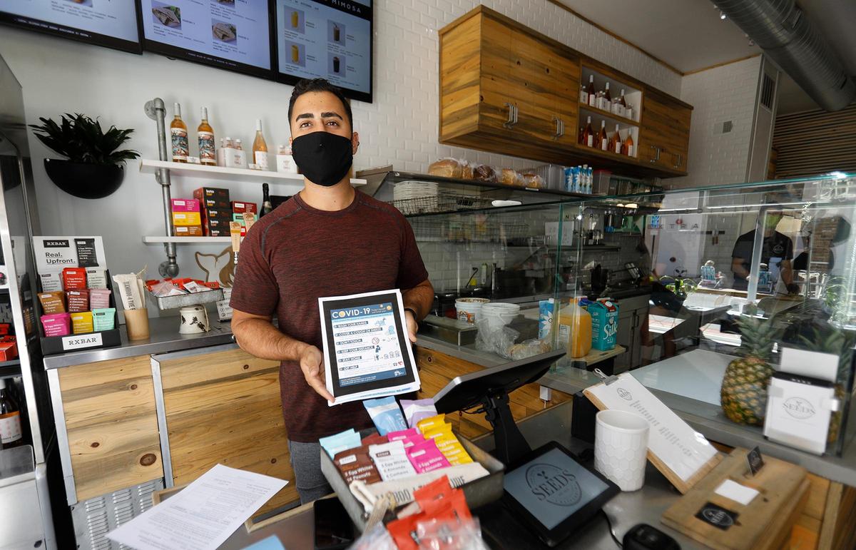 Downtown San Luis Obispo restaurants and businesses are slowly opening. Seed’s owner Rammy Aburashed holds some of the California Dept. of Health signs he has available in the store. The store opened Thursday.