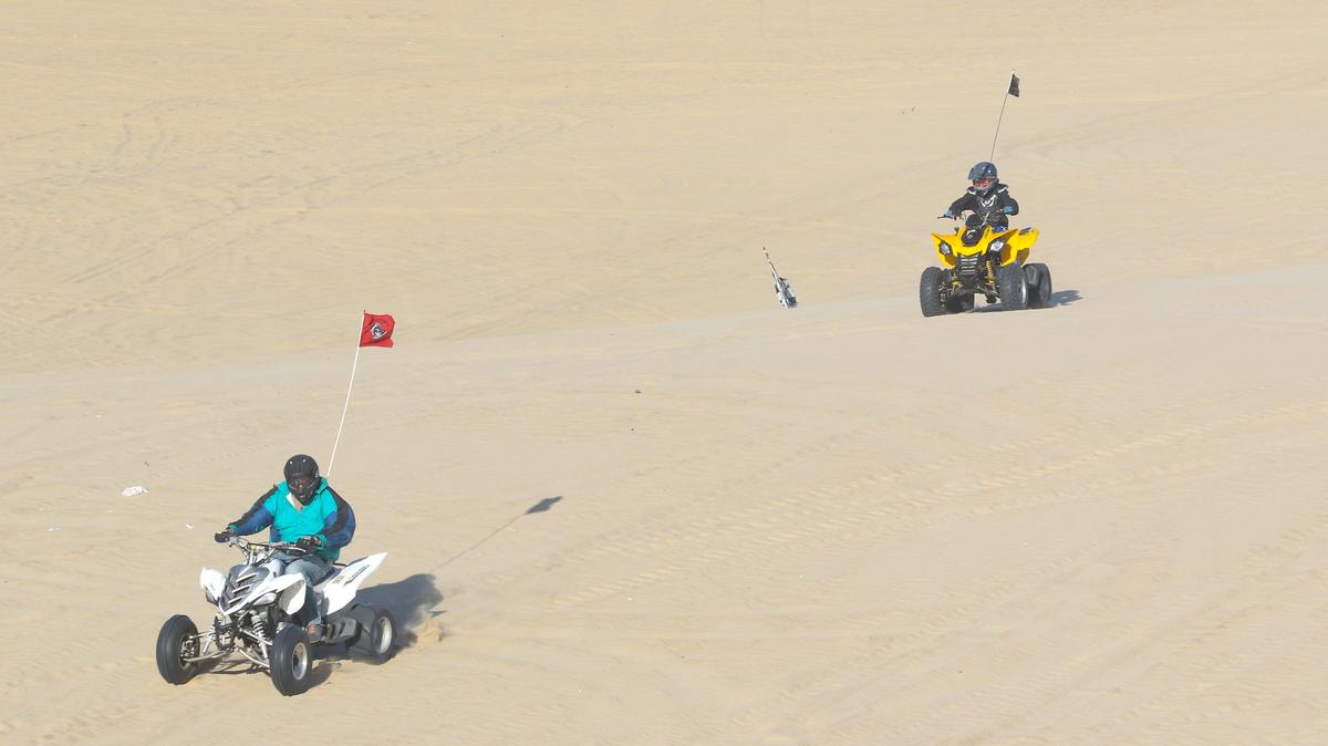 How many vehicles are in this photo? The third vehicle can be spotted by its flag, to the left of the yellow quad. The vehicle hidden behind a dune slope. Off road riders on the dunes on a summer evening at Oceano Dunes SRVA.