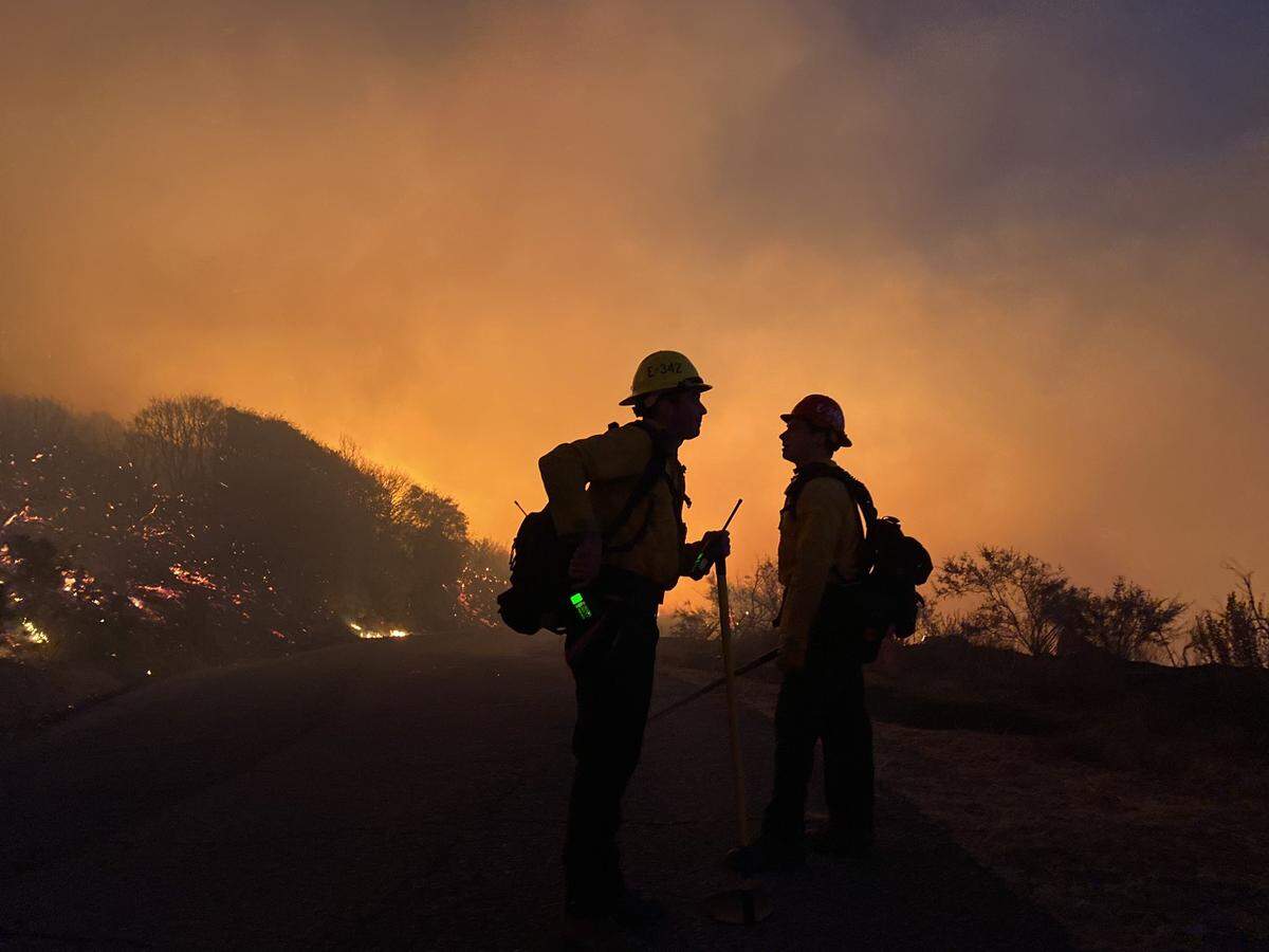 Firefighters at the Cave Fire backlit by flames.