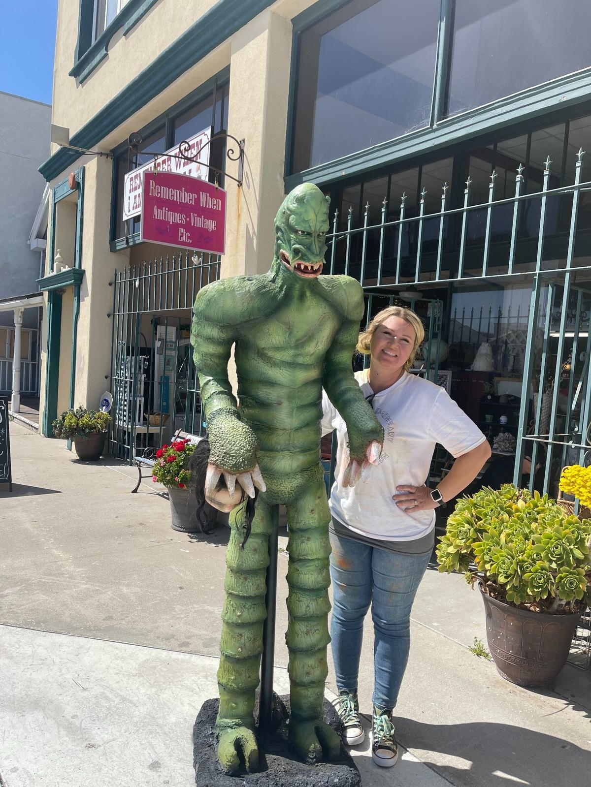 Jennifer Meiners, the owner of the antique shop Remember When in Cayucos, poses with a replica statue of the monster from the film “The Monster of Piedras Blancas.”