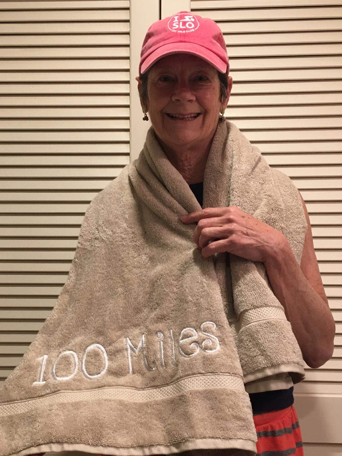 Retired San Luis Obispo therapist Linda Lewis Griffith celebrates swimming 100 miles in a year with a pink cap and a towel embroidered with the words “100 Miles.”