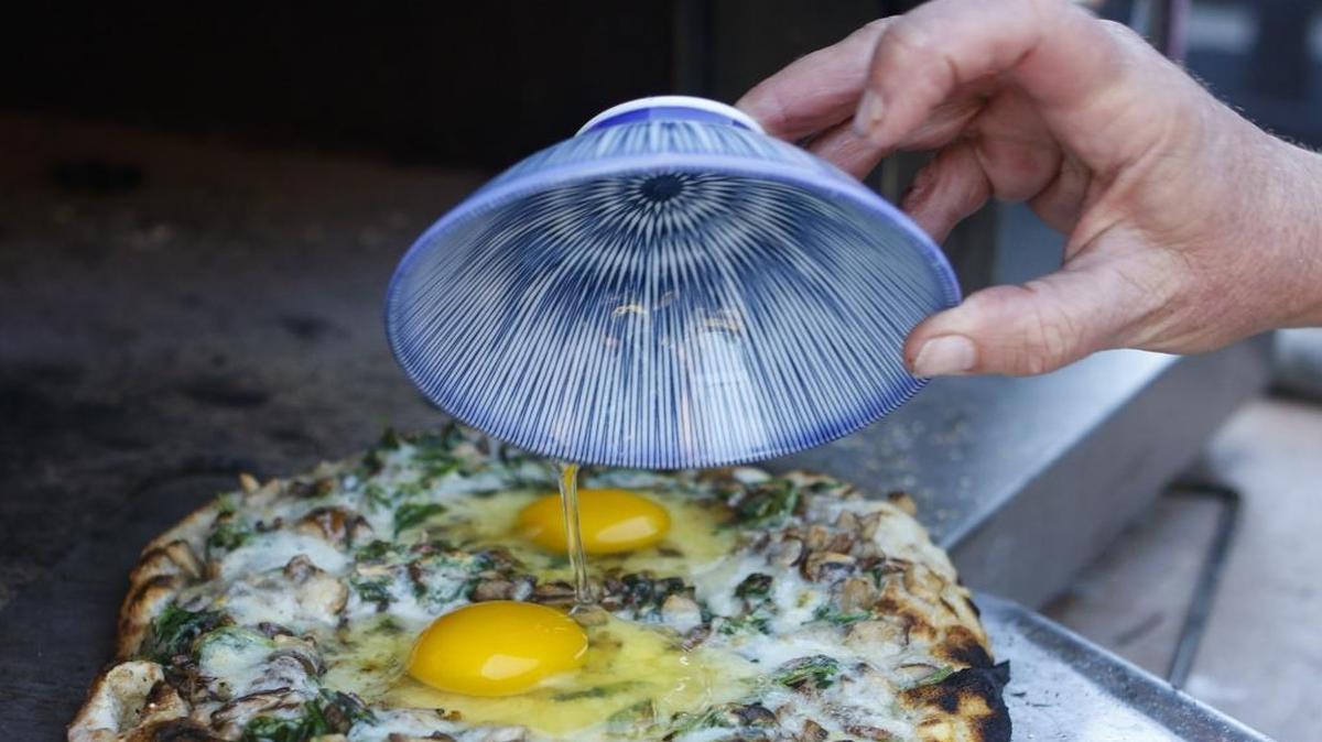 Farm-fresh eggs are added to a pizza topped with sautéed spinach, mushrooms and shallots at a “Art of Artisan Pizza” class at Refugio Kitchen in Paso Robles.