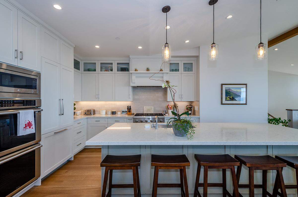 The kitchen of John and Dawn Turner’s Cayucos home features a textured tan tile backsplash and and a 10-foot-long island clad with gray-green quartz