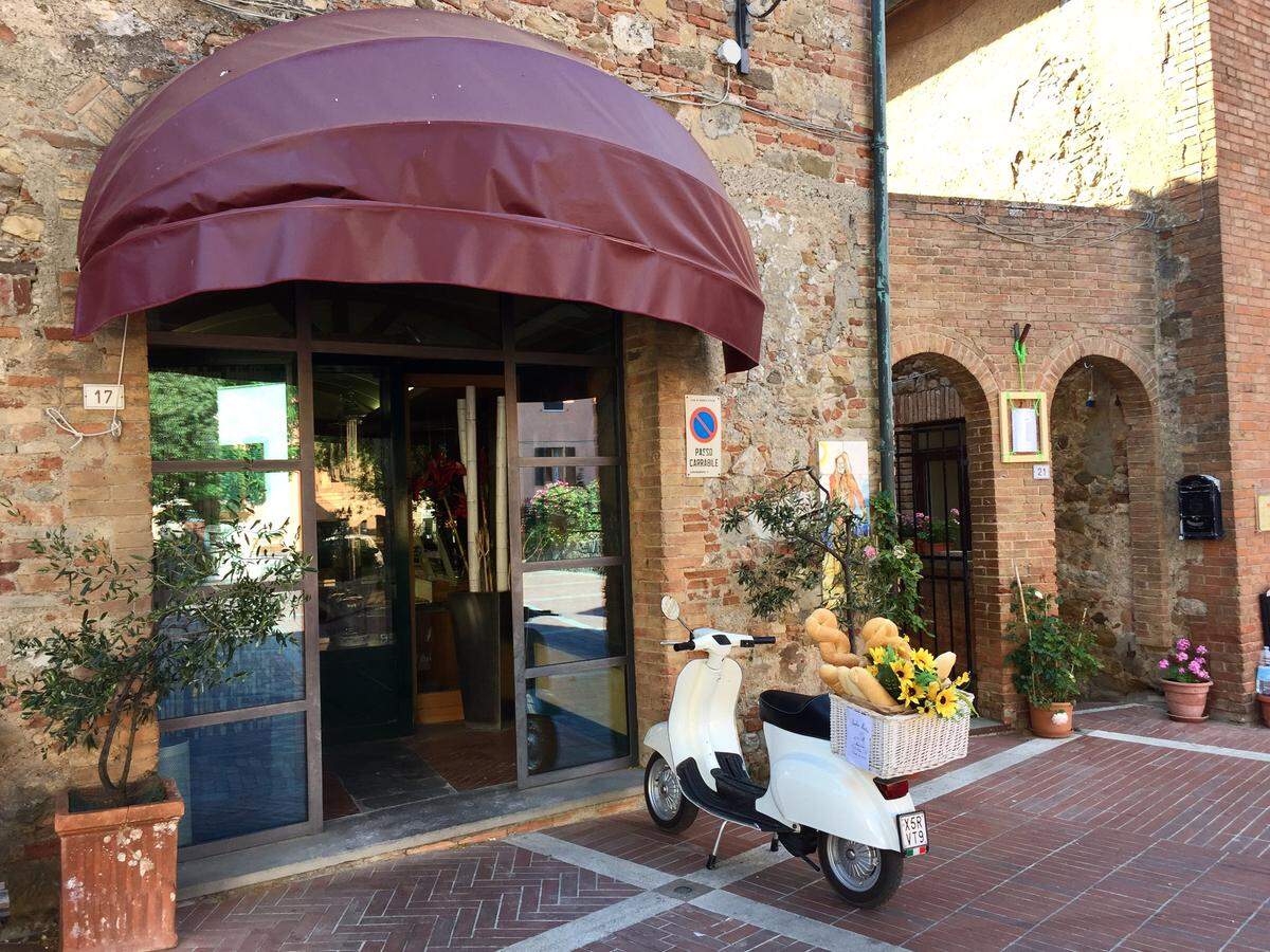 A Vespa bearing a basket of breads is parked outside a bakery in Casole d’Elsa, Italy.
