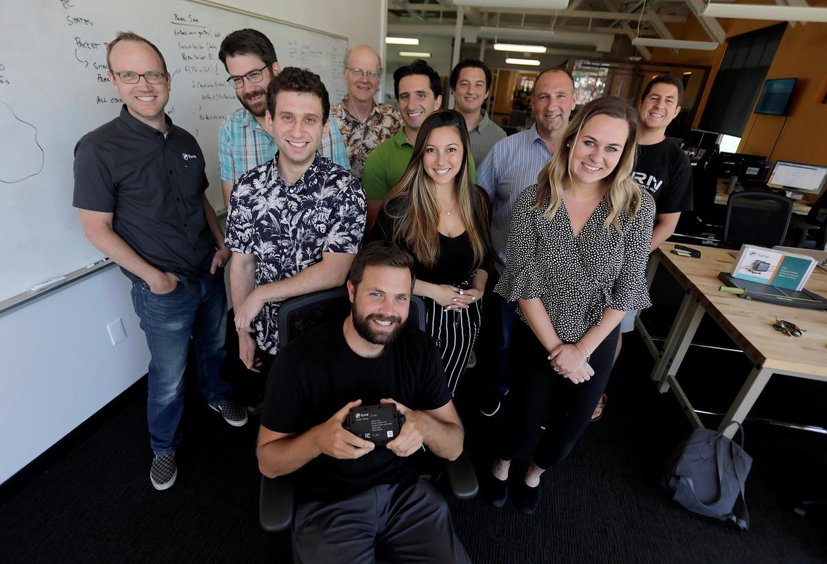 Flume co-founder James Fazio holds the Flume sensor flanked by the team of people who produce it in their San Luis Obispo office.
