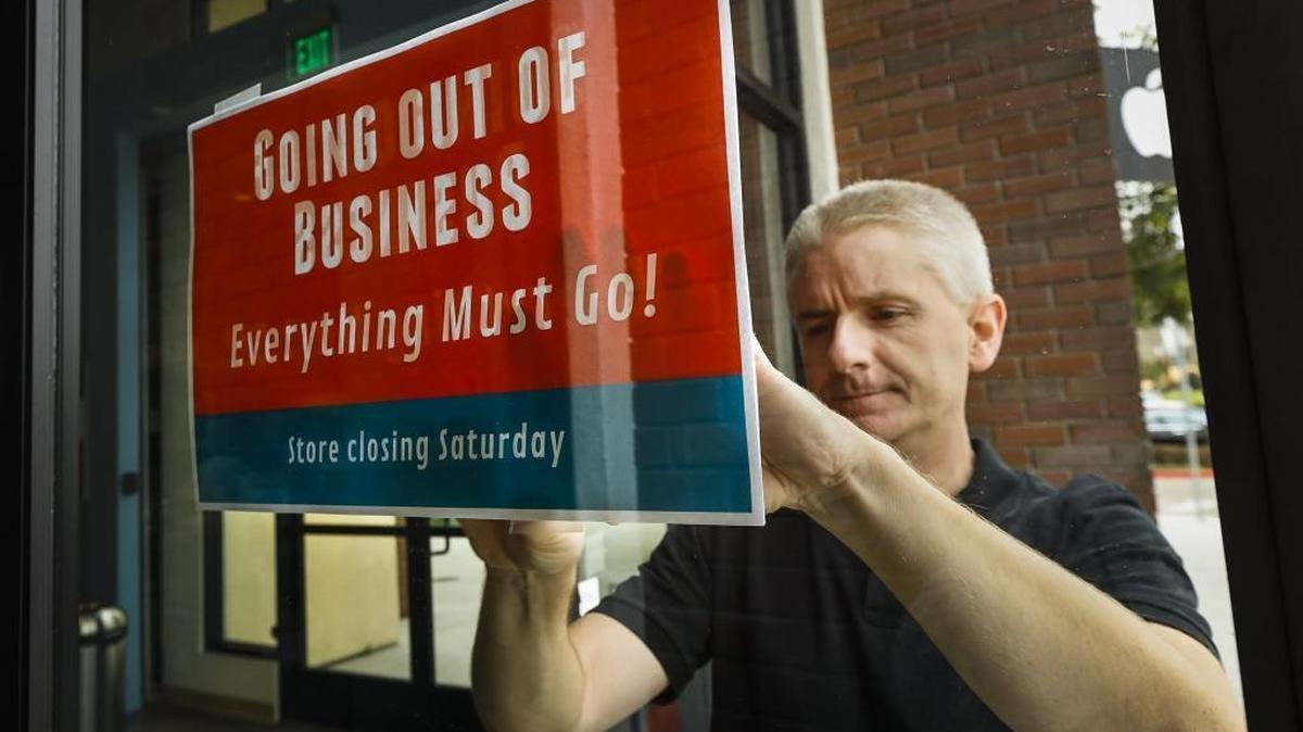 MacSuperstore owner Shane Williams tapes up a going out of business sign on the front of his store Monday.