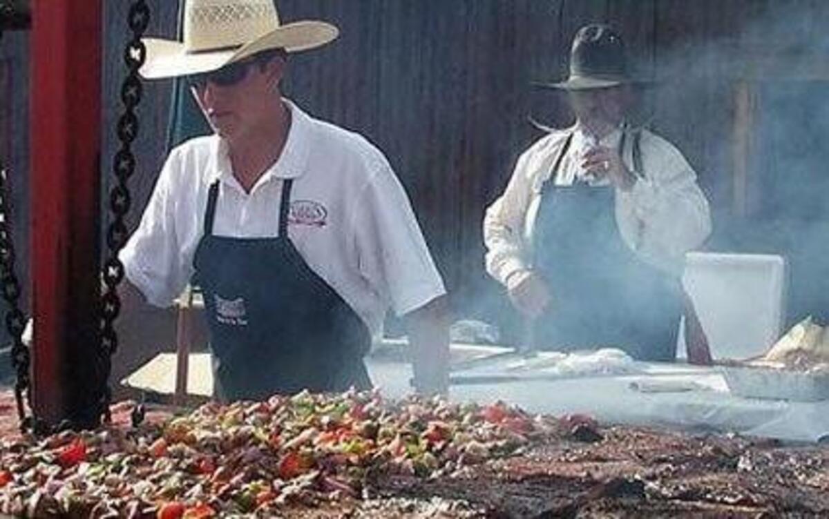 Billy Ruiz of Cowboy Flavor, at back, watches over a barbecue.