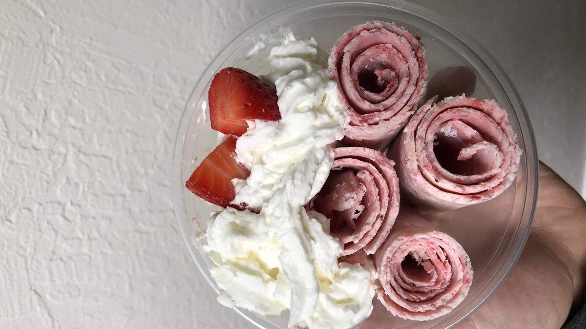 A dish of Rolld ice cream is served with whipped cream and strawberries.