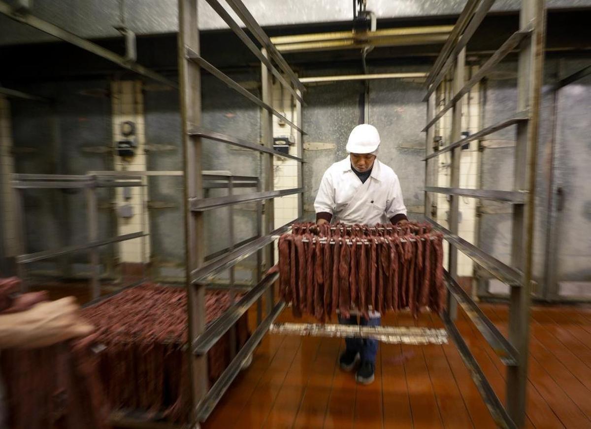 Luis Rios carefully hangs jerky on a cart that will be rolled into one of the ovens behind him to start the drying process at Cattaneo Bros. in San Luis Obispo.
